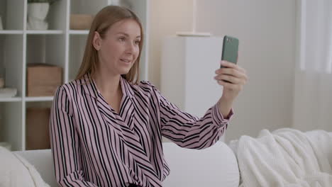 young woman is using video call in smartphone sitting at home and chatting with friends by internet during self-isolation