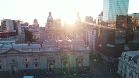 Aerial-view-sunset-passing-behind-Metropolitan-Cathedral-of-Santiago-bell-tower,-Plaza-de-Armas-district-of-Chile