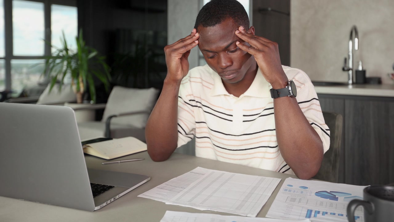 Stressed African American Man Working from Home with Laptop and Documents