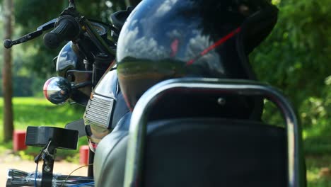 a helmet is placed on the back of an old motorbike , old indian motorbike sitting outdoors