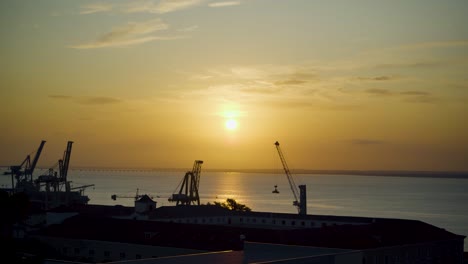 lisbon harbor sunrise with cranes silhouette through rusty fences