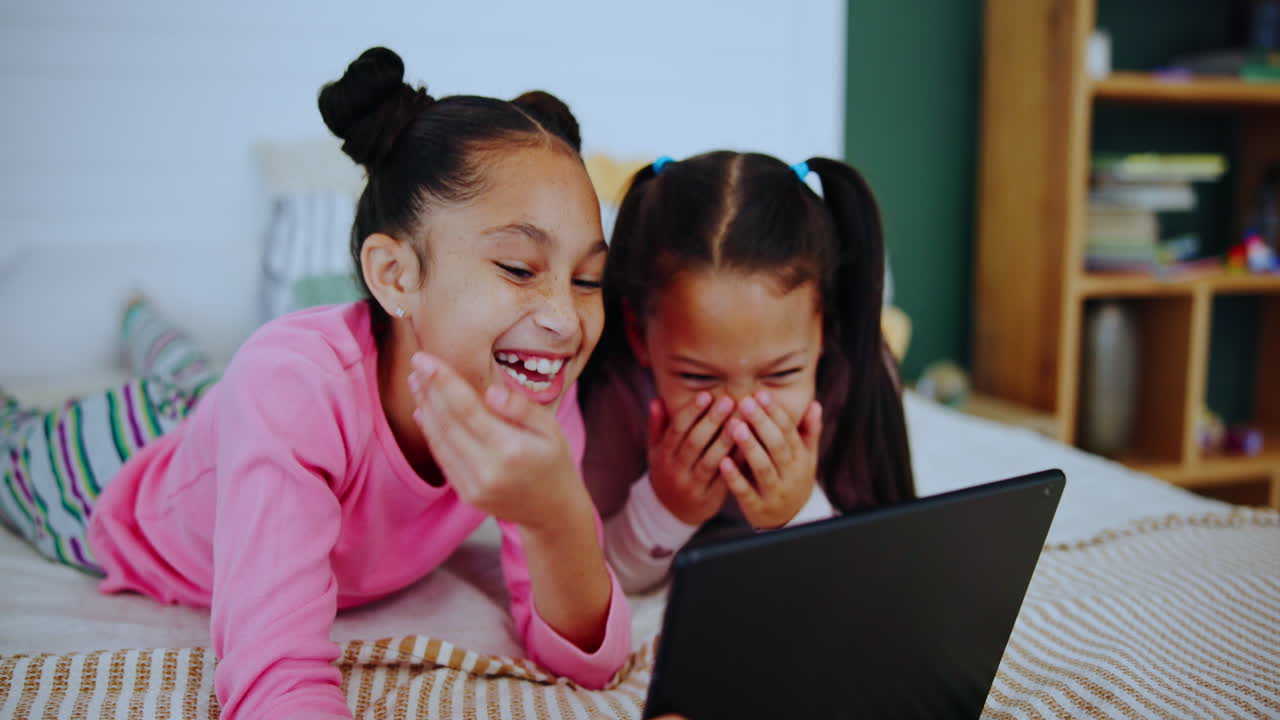 Two young girls using a tablet in the bedroom