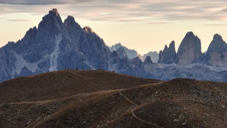 From-the-vantage-point-of-Toblacher-Pfannhorn-in-South-Tyrol,-the-sun-casts-a-soft-hue-over-the-imposing-Tre-Cime,-highlighting-its-grandeur