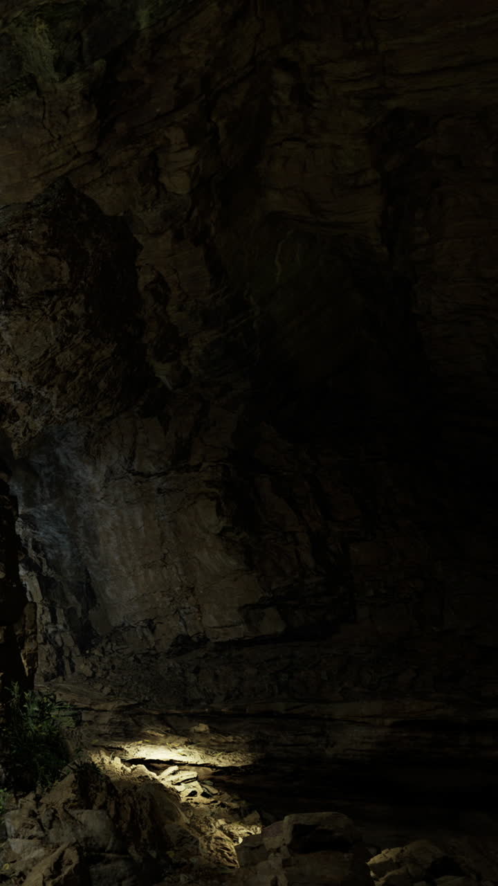 La luce si fa strada attraverso una grotta buia mostrando formazioni rocciose e ombre.