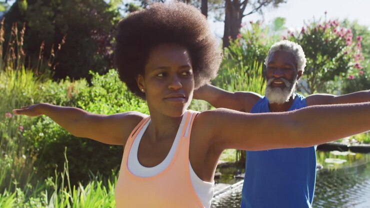 Coppia anziana afroamericana che pratica yoga in piedi in un giardino soleggiato