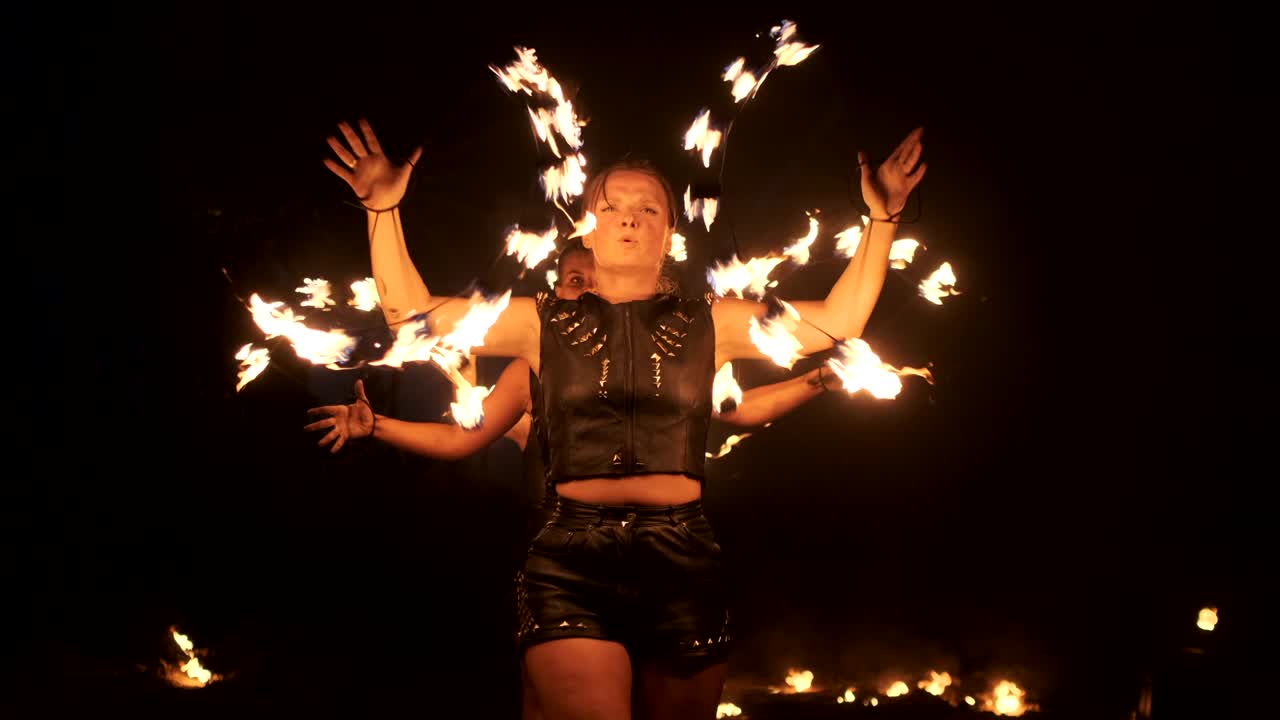tres mujeres con aros ardientes bailan con antorchas ardientes en ropa de cuero en un hangar oscuro demostrando un espectáculo de fuego de circo en cámara lenta.