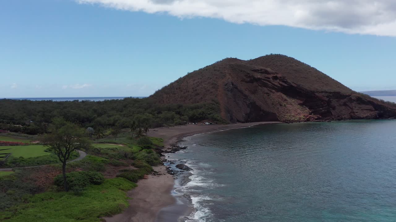 Low rising aerial shot flying over Maluaka Beach towards the cinder cone crater Pu'u Olai in South Maui, Hawai'i