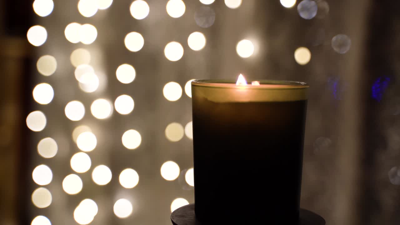 la vela de parofina brillante en vidrio arde por la noche sobre el fondo de las luces de gerlands