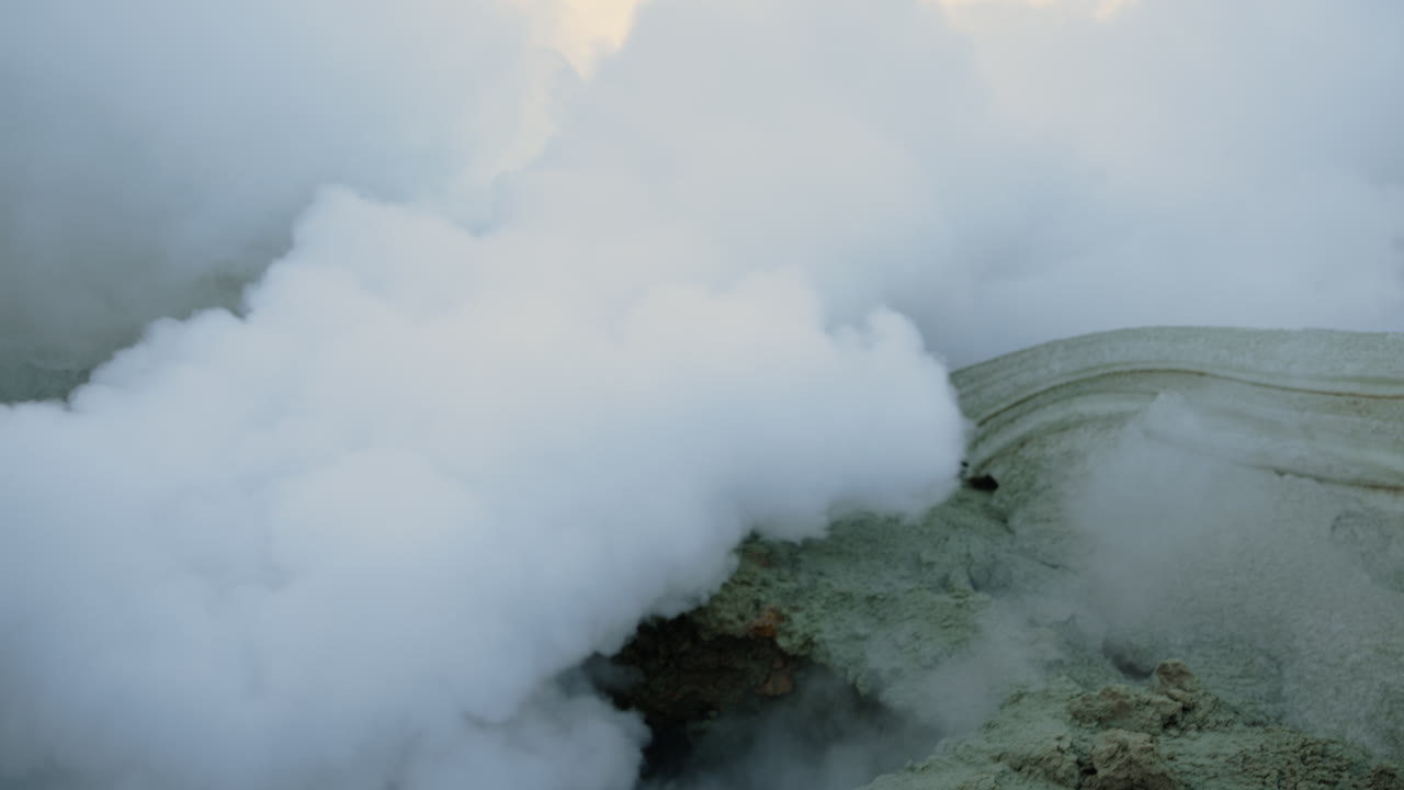 Espeso vapor subiendo de una fumarola geotérmica en terreno volcánico.