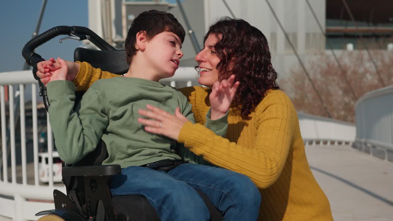 A mother lovingly embraces her disabled child in a wheelchair on a bridge