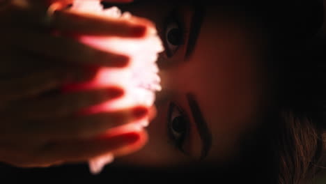 Close-up-shot-of-a-young-model-while-holding-a-bright-pink-colored-carnation-in-front-of-her-face-and-looking-at-the-camera