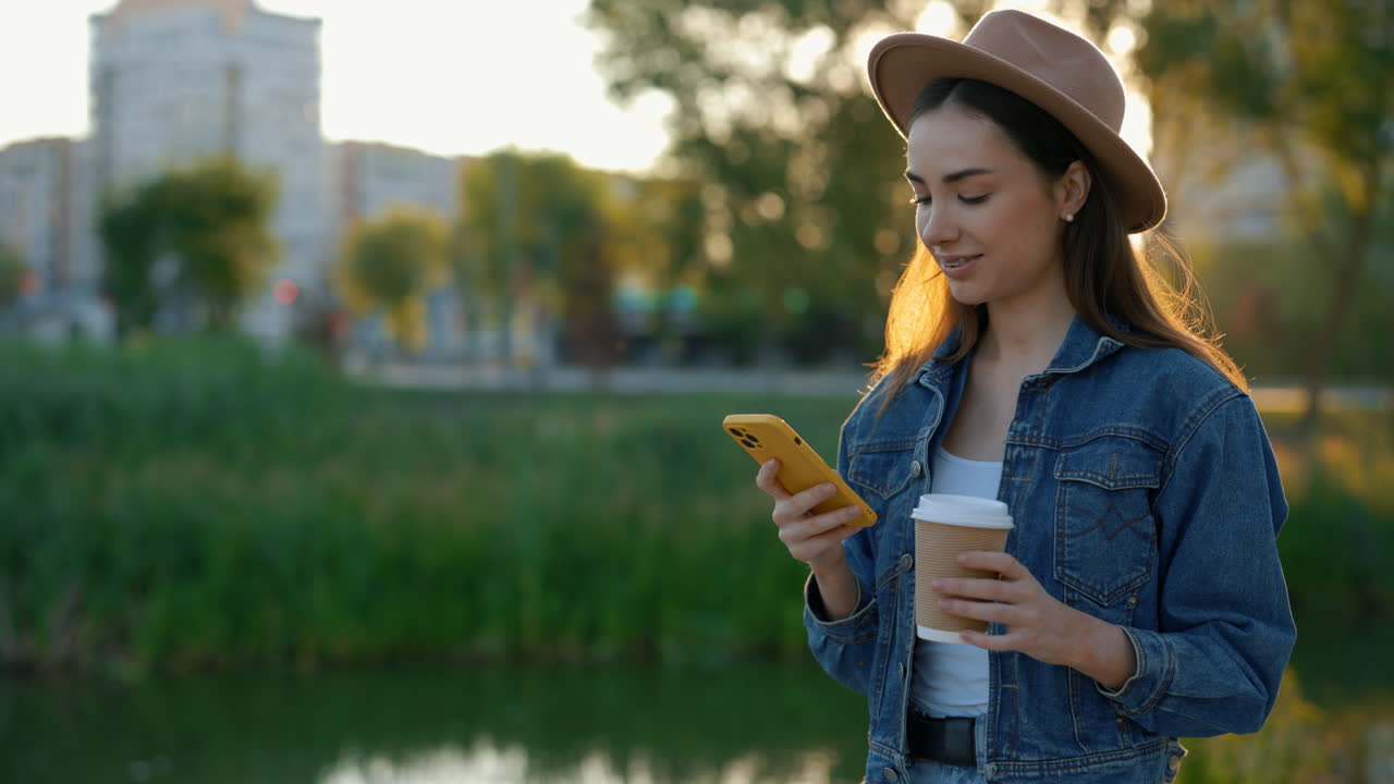 Young woman using phone outdoors with coffee