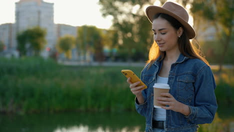 young woman using phone outdoors with coffee