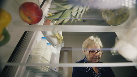 una anciana carga los productos en el refrigerador