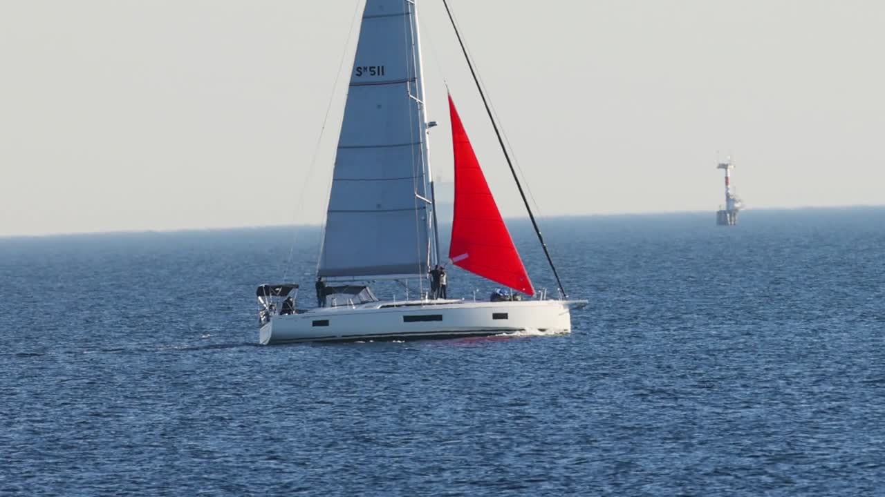 Una moderna barca a vela con una vivace vela rossa scivola su tranquille acque blu dell'oceano.