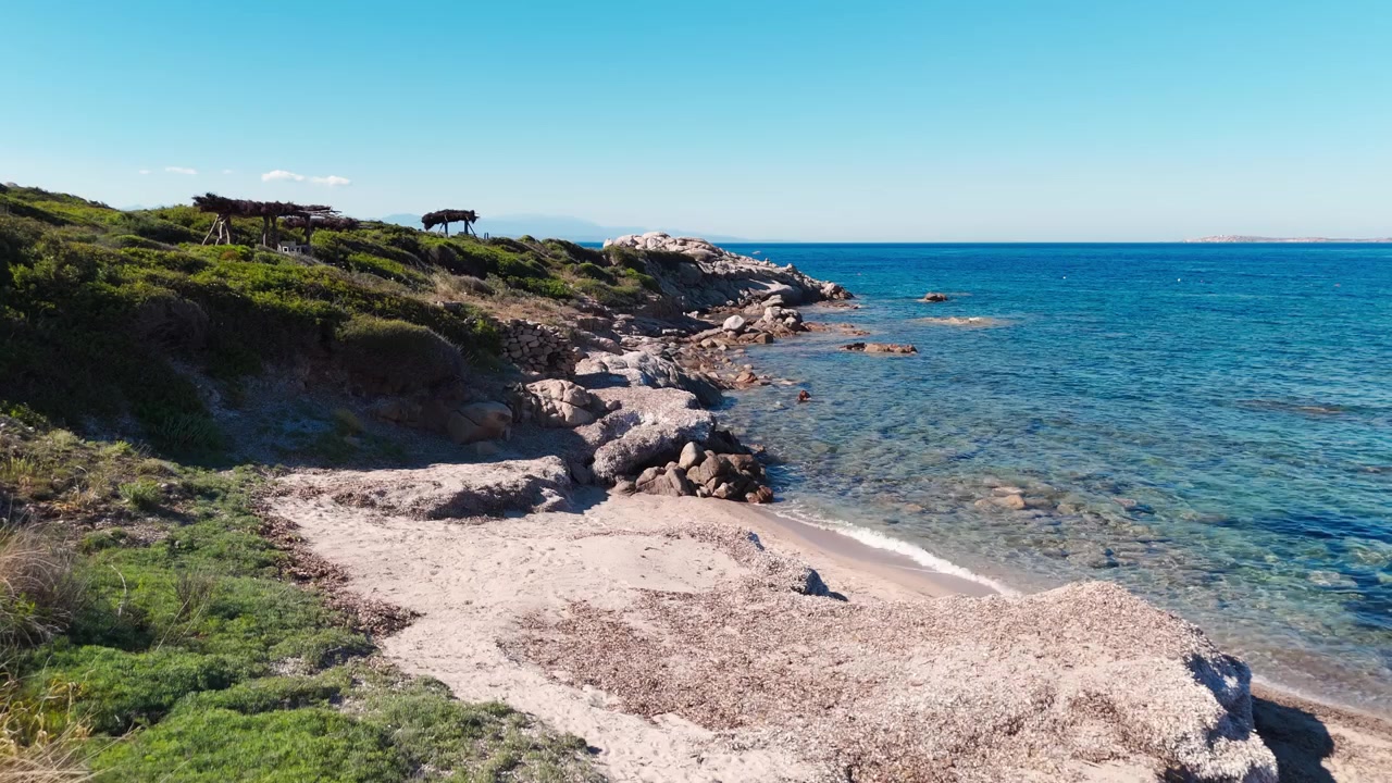 Veduta aerea di costa rocciosa e mare azzurro cristallino accanto a una spiaggia sabbiosa in Sardegna.