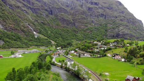 Aerial:-Flåm-train-going-through-a-valley-among-green-meadows-and-by-a-river-and-a-waterfall