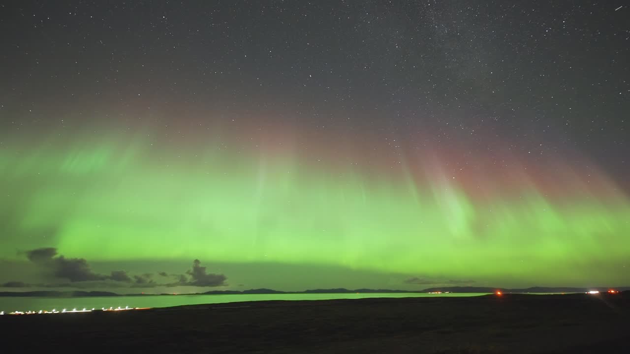 en una oscura noche de invierno, un fiordo tranquilo y su costa están iluminados por la encantadora danza de las luces del norte en este video timelapse