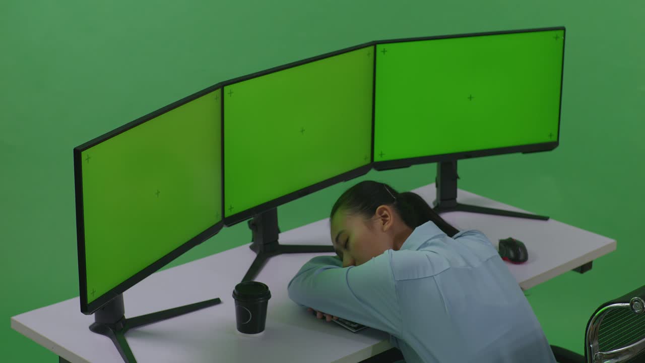 녹색 스크린 스튜디오에서 모의 여러 컴퓨터 모니터와 함께 작업하는 동안 잠을 자는 피곤한 아시아 여성의 측면 시각