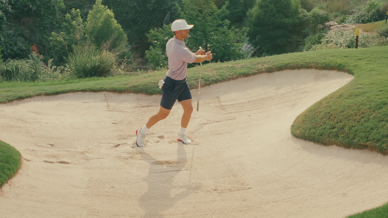 Male golfer hits a textbook bunker shot from a greenside sand trap in slow motion. Clean, smooth swing with sand flying as the ball lifts toward the green. Shot captures perfect short game execution.