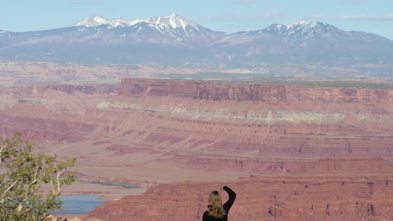 замедленная съемка женщины-туристки, показывающей рукой знак мира, на фоне вида из парка штата мертвая лошадь в штате юта, сша