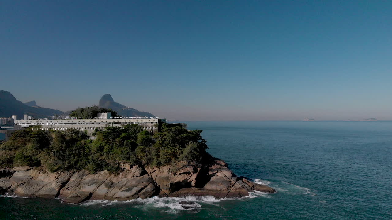 vista aérea de una pequeña isla con una construcción recreativa en la costa de río de janeiro que revela los famosos picos de la ciudad como el corcovado y la montaña dos hermanos al fondo