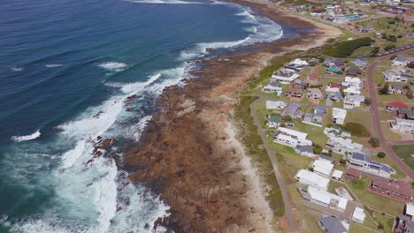 still bay aerial drone cinematic beach small surf town garden route south africa jeffreys bay homes and buildings waves crashing on reef late morning afternoon forward pan up movement