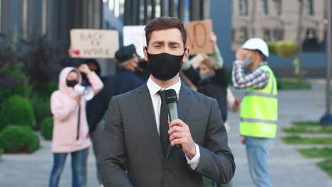 caucasian journalist or correspondent wearing protective mask giving interview in a protest against covid 19