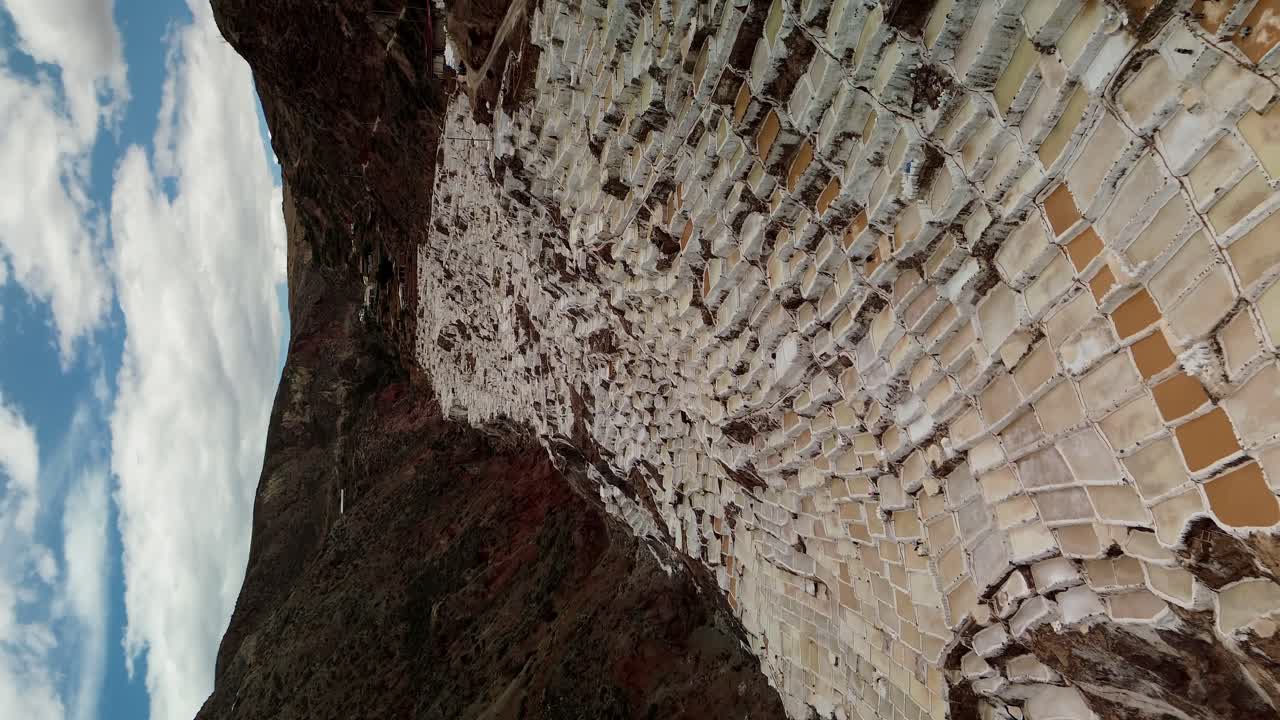 페루 마라스의 소금 테라스, 구름이 가득한 하늘과 바위 풍경을 배경으로