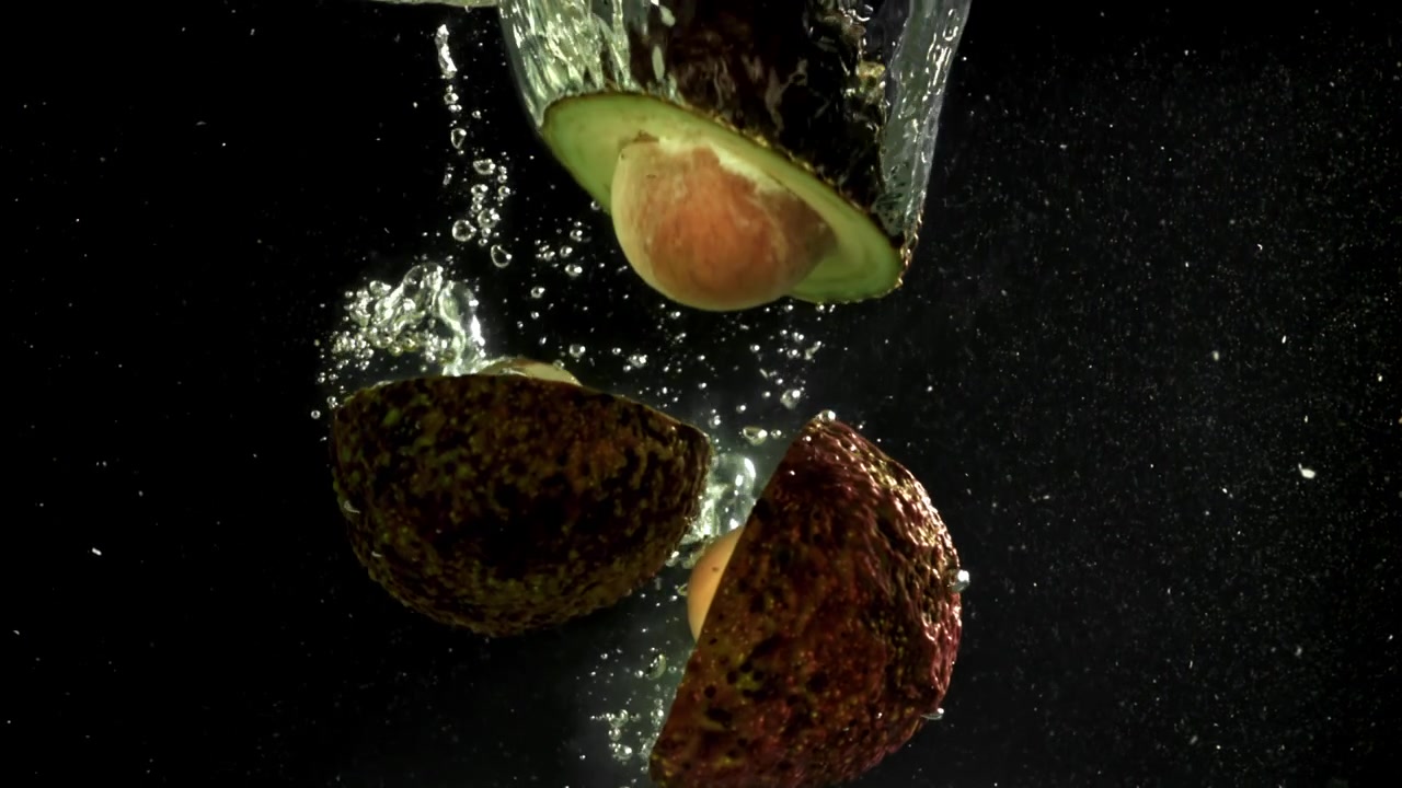 Metà di avocado e nocciolo che cadono nell'acqua con bolle