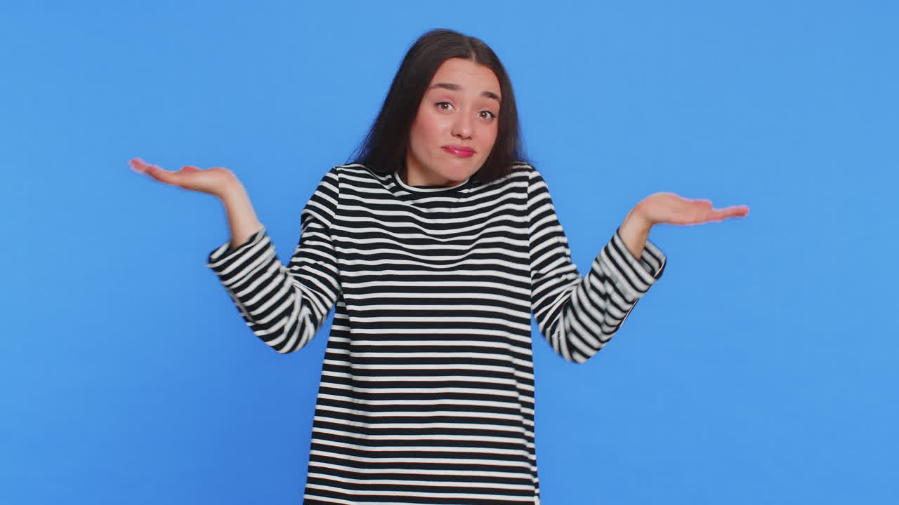 Confused Young Woman Shrugs and Scratches Head on Blue Background