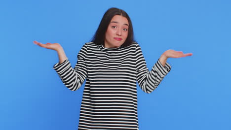 confused young woman shrugs and scratches head on blue background
