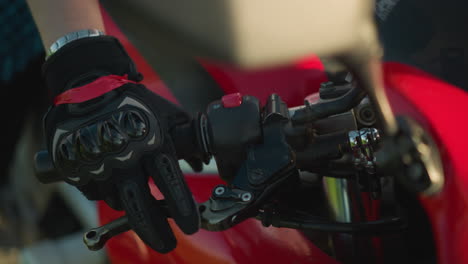 close-up of a biker's hand wearing protective gloves while gripping the throttle and clutch lever on a motorcycle, the rider's wrist is adorned with a chain bracelet