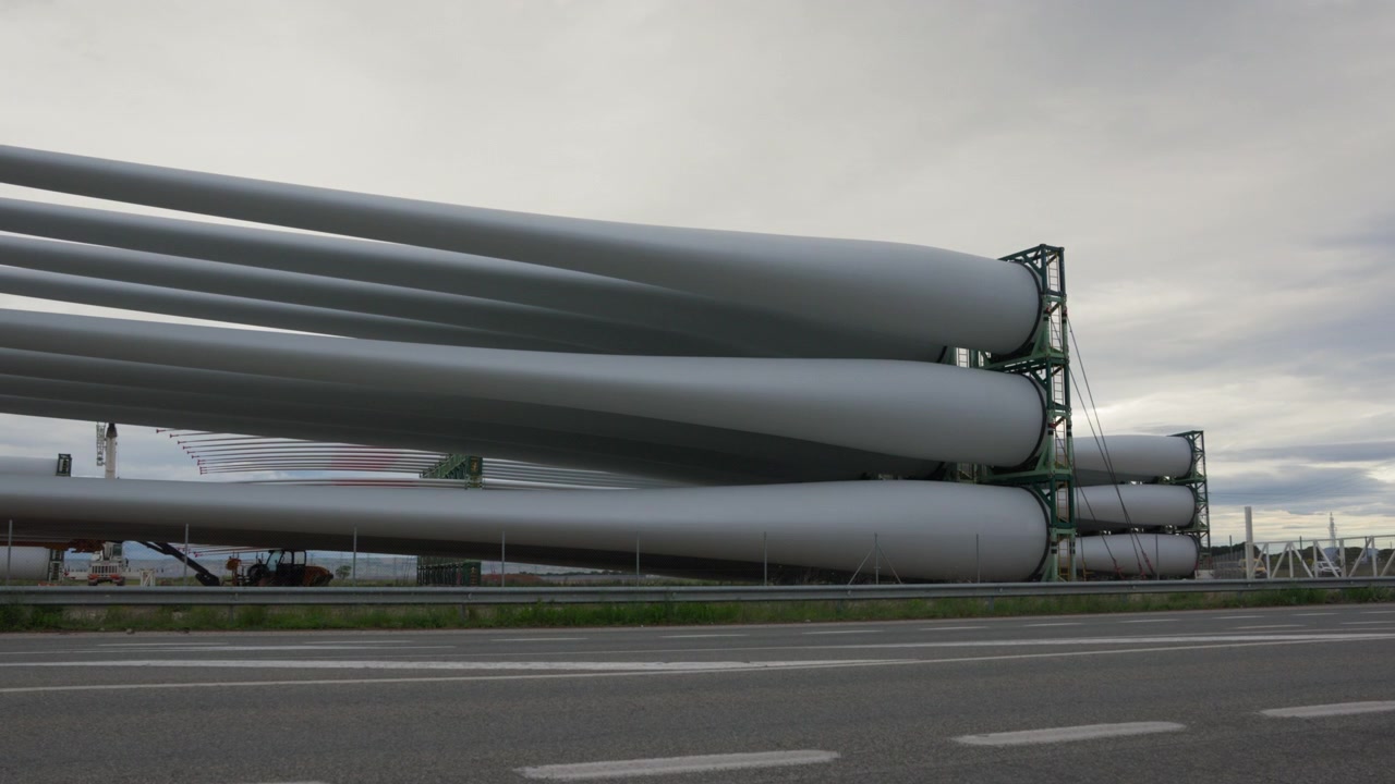 Grandi pale di turbine eoliche stoccate a lato di un'autostrada con veicoli in transito