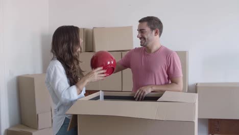 Happy-couple-unpacking-cardboard-boxes-with-stuff,-talking-and-smiling