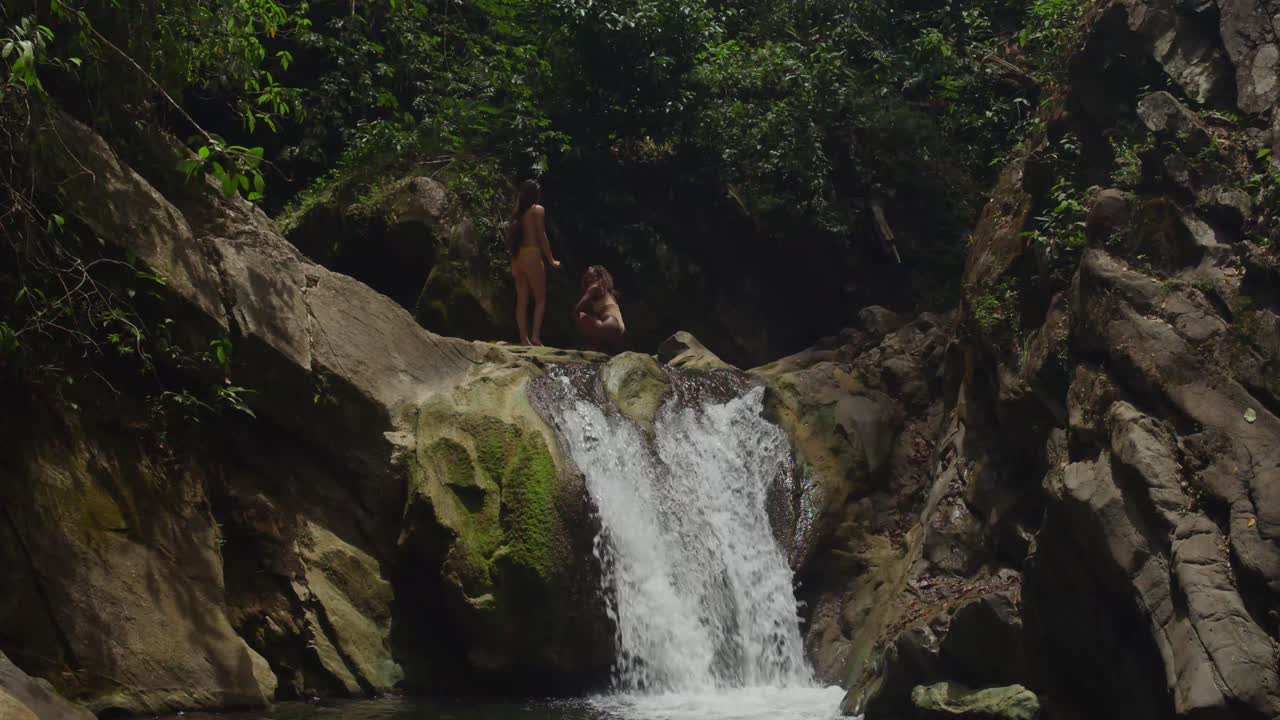 Two girls in bikinis are captivated by a tropical waterfall and river in the Caribbean.