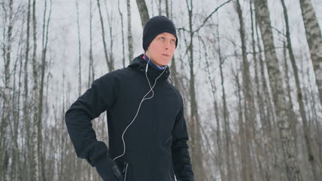 Ein-Junger-Mann-In-Einem-Schwarzen-Hammer-Bereitet-Sich-Im-Winter-Auf-Das-Joggen-Im-Park-Vor,-Enthält-Eine-Laufanwendung-Und-Rennt-Mit-Einem-Sprachassistenten-Durch-Den-Wald,-Um-Geschäfte-Zu-Machen-Und-Einen-Gesunden-Lebensstil-Zu-Führen.