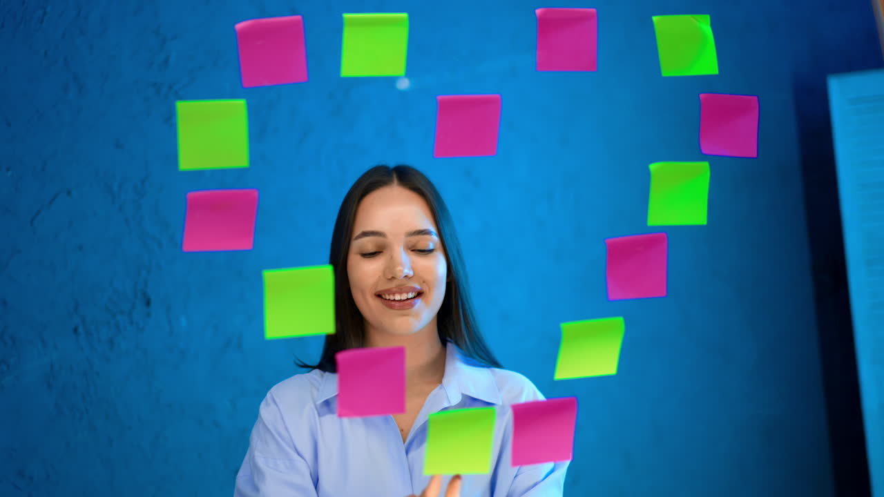 Beautiful brunette lady looks at stickers on the glass board. Smiling girl points at stickers in a shape of heart and shows heart sign with her hands.