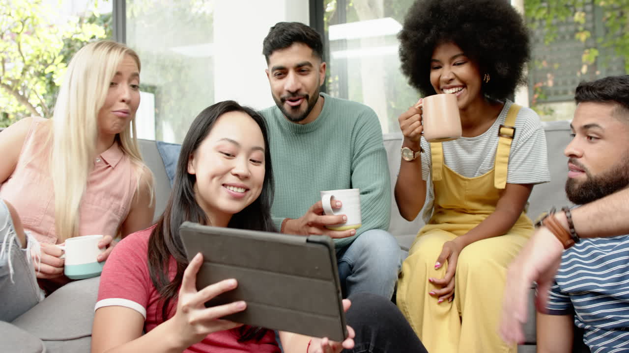 Watching video on tablet, group of young friends relaxing and smiling together