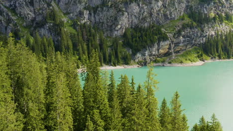 Drone-flying-over-tree-tops-towards-a-beautiful-blue-lake