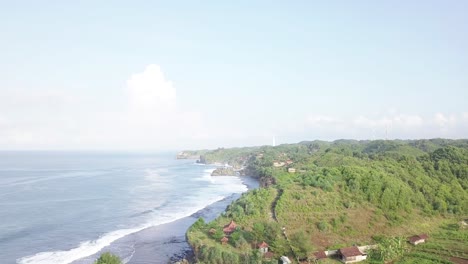 Drohnenflug-über-Den-Südstrand-Der-Insel-Java-In-Indonesien,-Als-Am-Morgen-Die-Ersten-Sonnenstrahlen-Die-Grünen-Küstenberge-Trafen