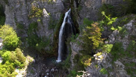 Vista-Aérea-Cinematográfica-De-La-Cascada-Con-Agua-De-Arroyo-Salvaje-Que-Cae-De-La-Montaña-Rocosa-En-Theth,-Albania