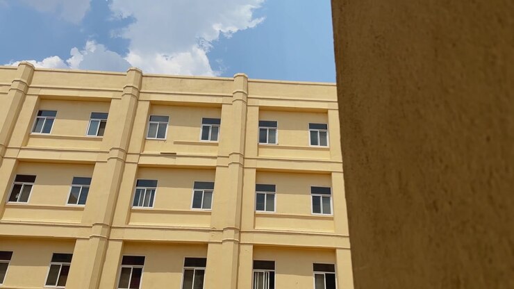 Carrellata che rivela un edificio multipiano di nuova costruzione con architettura moderna, facciata pulita sotto un cielo luminoso, adatto per l'istruzione, l'amministrazione sanitaria o i servizi giudiziari.