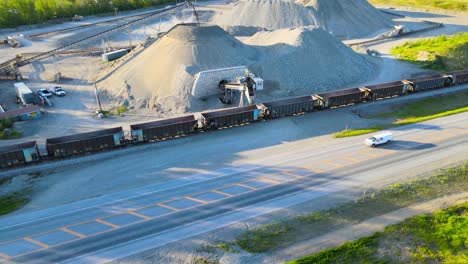 View-from-above-of-train-loading-up-with-gravel-as-camera-pans-upward-to-reveal-snowy-mountains-in-the-background