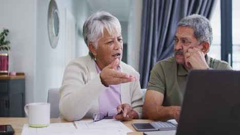 Senior-biracial-couple-talking-and-using-laptop