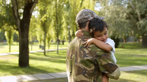 feliz pai militar segurando o filho nos braços ao ar livre