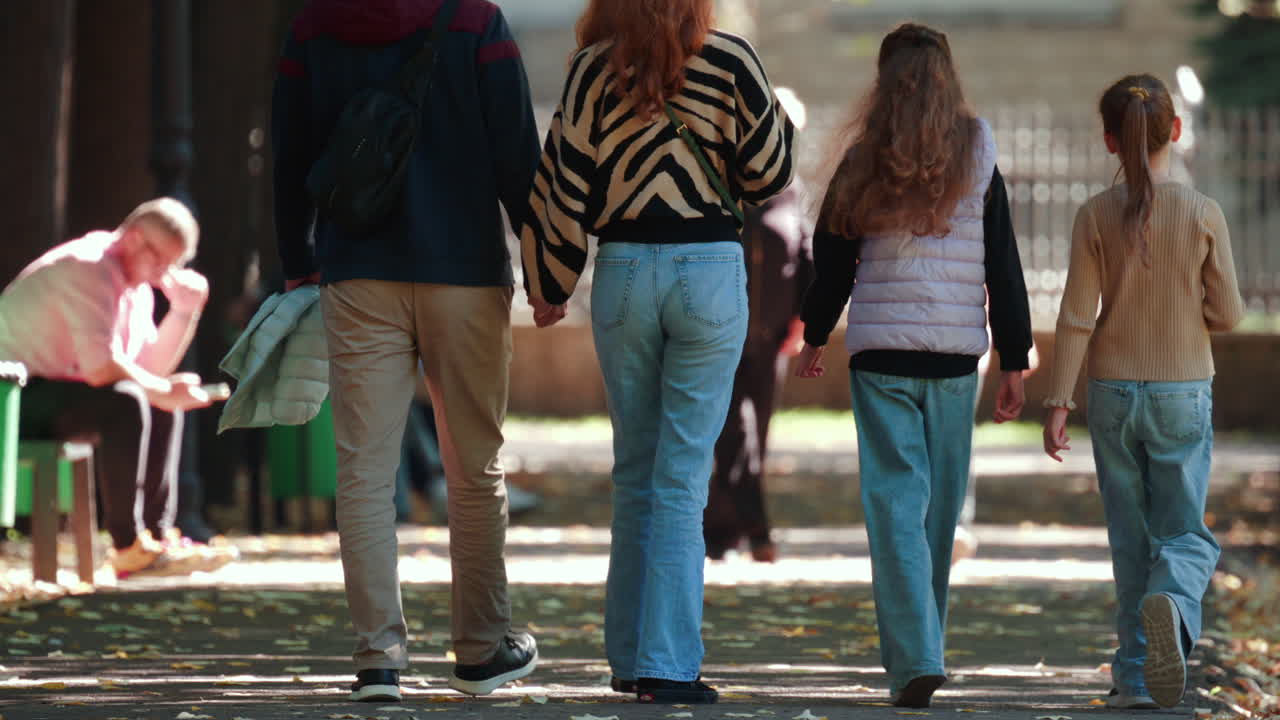 Back view of a family strolling hand in hand through a park on a sunny autumn afternoon