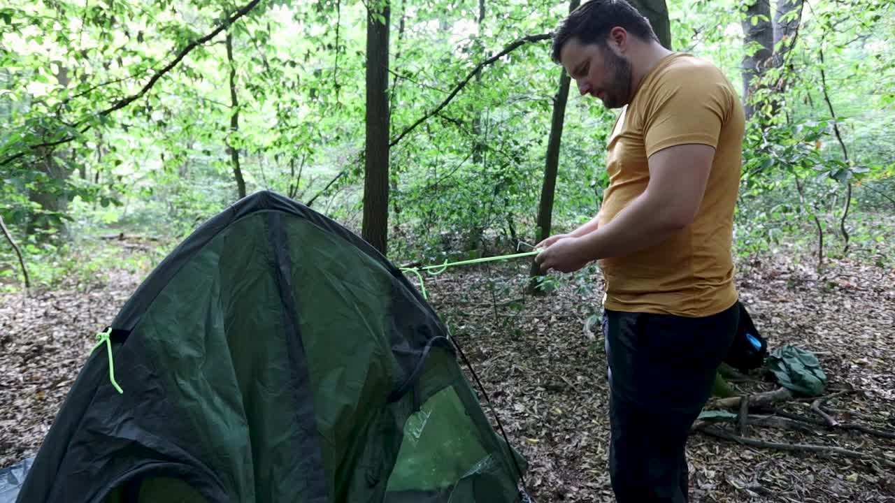 Man pitches a tent and ties the ropes at a campsite in the forest