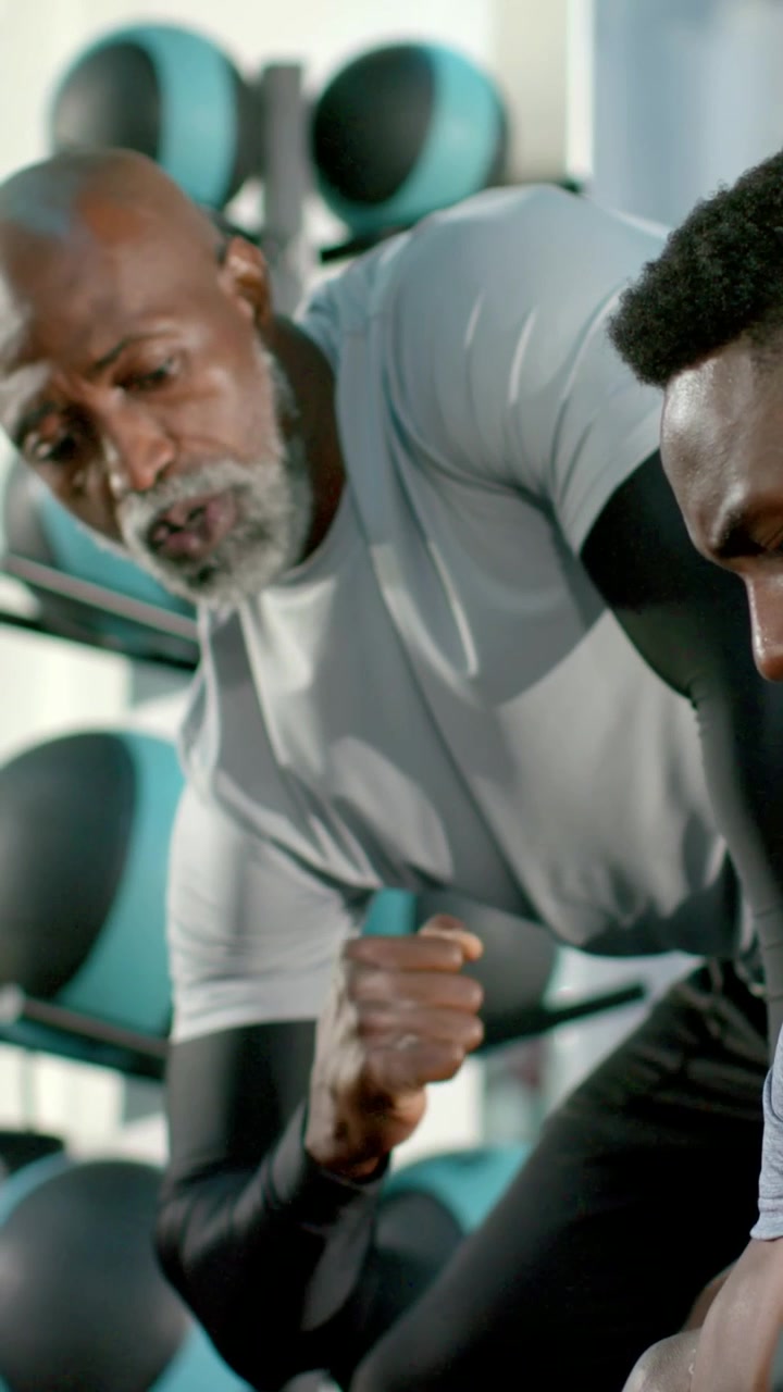 Vertical video: Leaning coach giving fist cues, counting client curling dumbbell in sleeves at gym