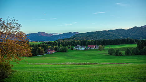 Tima-lapse-of-the-picturesque-landscape-with-green-meadow-at-attersee-lake-in-austria-with-a-view-of-traditional-austrian-houses-with-red-roofs-and-the-forested-mountains-and-peaks